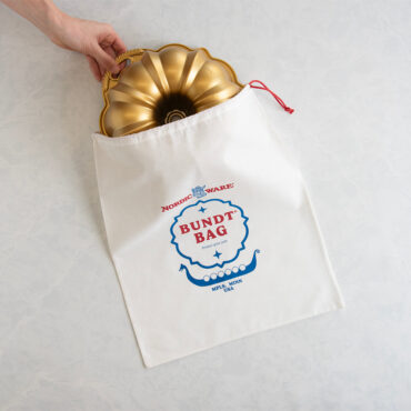 Hand removing fluted aluminum bundt pan from gray Nordic Ware drawstring storage bag