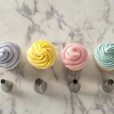 Four cupcakes with white frosting piped using different decorating tips showing rosette, star, leaf, and round designs