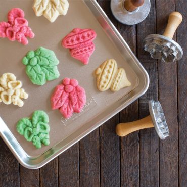 Nordic Ware aluminum baking sheet with colorful stamped sugar cookies in leaf, acorn, and tree shapes