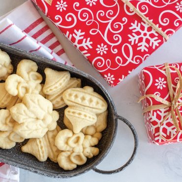 Golden pressed holiday cookies in dark metal baking tray with red and white snowflake gift boxes