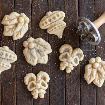 Baked sugar cookies cut into holiday shapes with detailed stamped patterns on dark wood surface