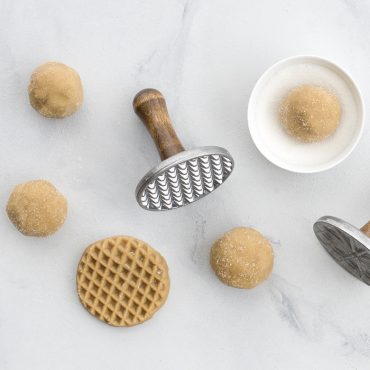Nordic Ware wooden cookie stamps beside peanut butter cookie dough balls and stamped cookies with decorative patterns