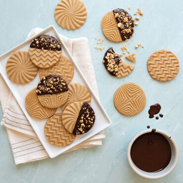 Geometric-shaped cookies, some plain and others chocolate-dipped, displayed on white plate and marble surface