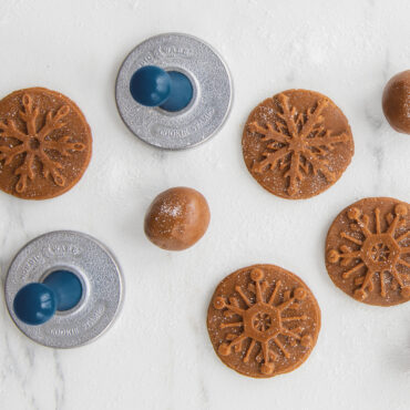 Raw cookie dough with detailed snowflake impressions from Nordic Ware cookie stamps on floured surface