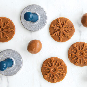 Raw cookie dough circles stamped with detailed snowflake patterns using Nordic Ware cookie stamps on floured surface