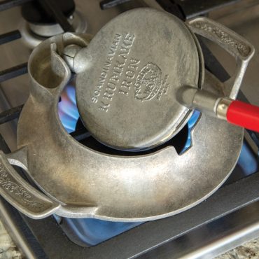 Nordic Ware krumkake iron with handles being pressed together, showing cooking technique step with timer indication