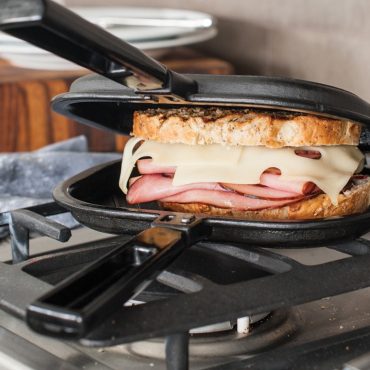 Cast iron grill press compressing golden-brown grilled ham and cheese sandwich on stovetop griddle