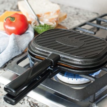 Nordic Ware aluminum sandwich grill press on gas stovetop, rectangular with hinged lid and black handles
