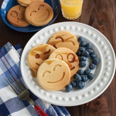 Golden smiley face pancakes with blueberry eyes and bacon smile on white plate, made with Nordic Ware pancake pan