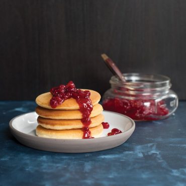 Stack of golden mini pancakes topped with red lingonberry jam, made using Nordic Ware silver dollar pancake pan