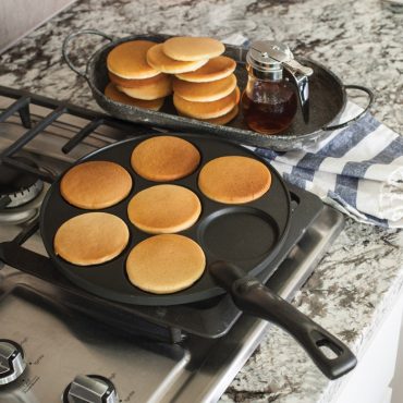 Nordic Ware silver dollar pancake pan with golden mini pancakes cooking, stack of finished pancakes on plate