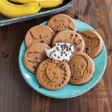 Six golden animal-shaped pancakes arranged on white plate with dollop of whipped cream, made with Nordic Ware Zoo Friends pan