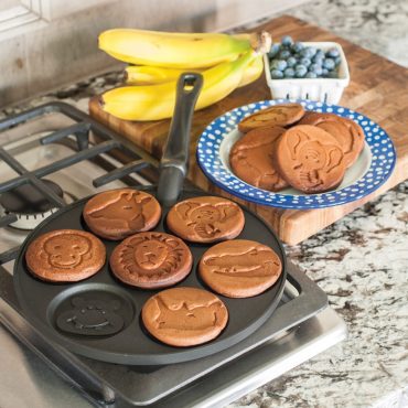 Nordic Ware Zoo Friends cast aluminum pancake pan on stovetop with six golden animal-shaped pancakes