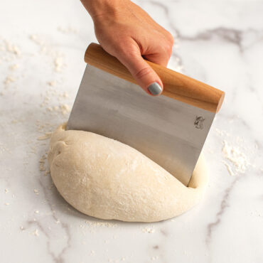 Nordic Ware stainless steel dough scraper cutting through white bread dough on floured surface
