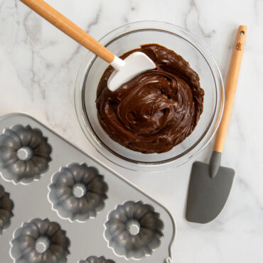 Two Nordic Ware silicone spatulas - white one mixing cake batter in bowl, grey one beside mini bundt pan