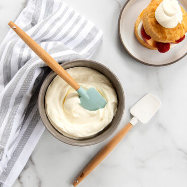 Two small white Nordic Ware spatulas with biscuits, berries, and whipped cream on wooden surface