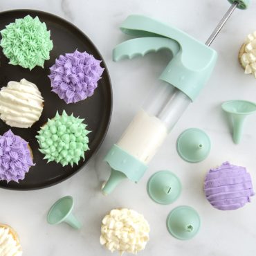 Six cupcakes with elaborate white frosting decorations made using Nordic Ware decorating tips and spritz maker