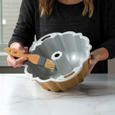 Person preparing Nordic Ware Anniversary bundt pan with natural bristle pastry brush and baking spray