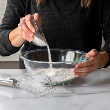 Nordic Ware large stainless steel whisk beside glass mixing bowl filled with white flour on counter