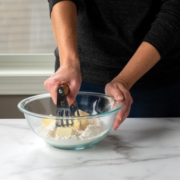 Nordic Ware stainless steel pastry blender with black handle cutting butter into flour mixture in glass bowl