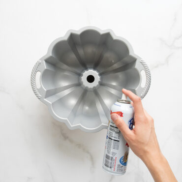 Hand spraying Baker's Joy nonstick baking spray into fluted aluminum bundt pan