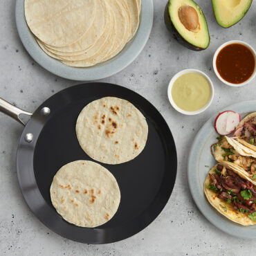 Nordic Ware black steel crepe pan with golden tortillas, plated tacos with avocado slices, overhead view