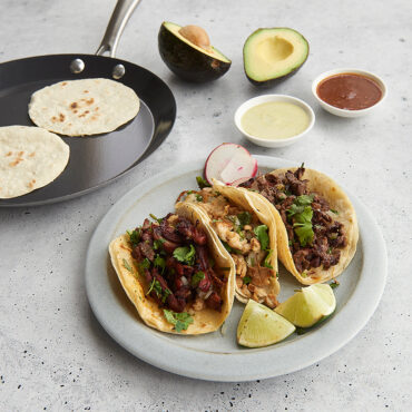 Nordic Ware blue steel crepe pan with golden crepe, alongside plated tacos with avocado slices