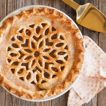 Golden-brown baked pie with decorative lattice heart pattern crust topping, showing fluted pie dish edge