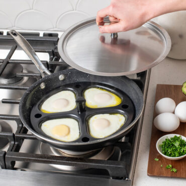 Nordic Ware nonstick egg poacher insert in silver pan on stovetop, hand holding lid, eggs cooking in individual cups