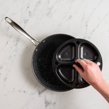 Hand placing Nordic Ware nonstick egg poacher insert with four cups into stainless steel pan, overhead view