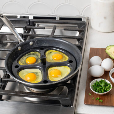 Nonstick egg poacher insert in stainless steel pan on stovetop, four raw eggs in individual cups ready to cook