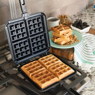 Nordic Ware stovetop Belgian waffler with hinged aluminum plates, golden square waffles cooking inside