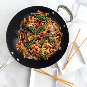 Nordic Ware 14-inch spun aluminum wok with colorful vegetable stir-fry, dark nonstick interior, steel handles