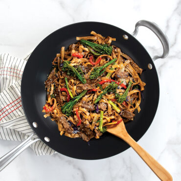 Nordic Ware 14-inch black spun aluminum wok with colorful vegetable stir-fry and wooden spoon