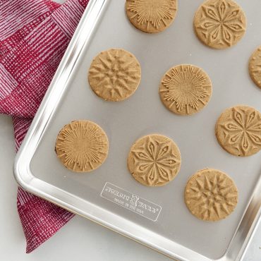 Golden baked cookies with star, moon, and celestial patterns stamped on surface, arranged on parchment-lined baking sheet