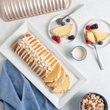 Golden glazed almond cake in Nordic Ware's detailed aluminum loaf pan, topped with sliced almonds