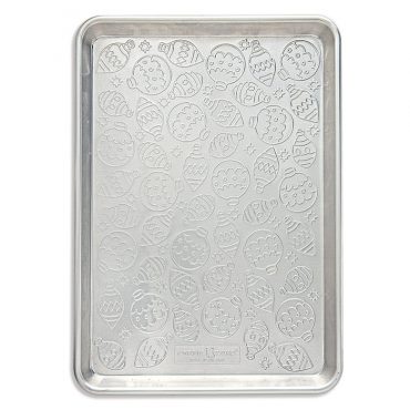Nordic Ware aluminum half sheet pan with embossed tree ornament pattern, displaying decorated sugar cookies