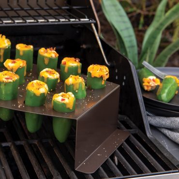 Grilled jalapeño peppers stuffed with cheese in Nordic Ware aluminum roasting stand on outdoor grill