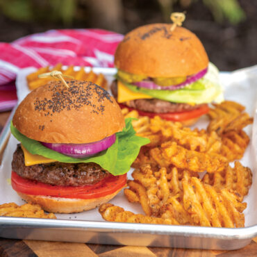 Nordic Ware aluminum cheese melting dome covering hamburger on grill, silver dome-shaped lid melting cheese