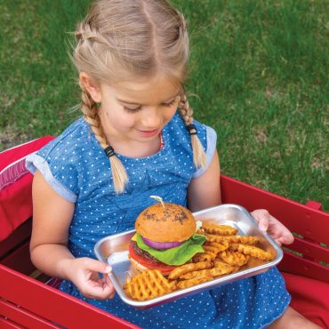 Child in red wagon holding white Nordic Ware burger serving tray with hamburger and waffle fries