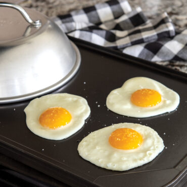 Nordic Ware aluminum cheese melting dome on griddle with melted cheese on burger patties