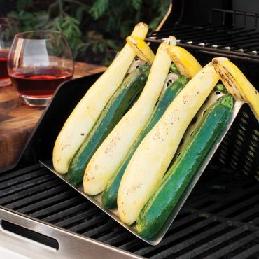 Nordic Ware aluminum grill tent holding three halved zucchini with seasoning, positioned on black grill grates