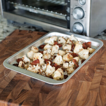 Golden roasted cauliflower florets on Nordic Ware aluminum compact baking sheet, natural silver finish
