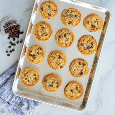 Freshly baked chocolate chip cookies on Nordic Ware aluminum half sheet pan, golden brown with crispy edges