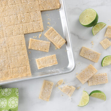 Square shortbread bars dusted with powdered sugar and lime wedges on Nordic Ware aluminum half sheet pan