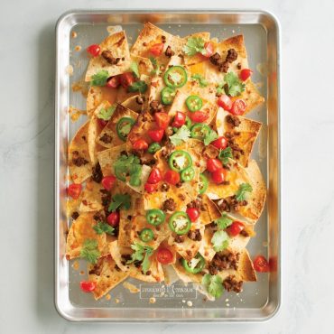 Nordic Ware aluminum jelly roll pan with loaded nachos topped with cheese, jalapeños, and cilantro