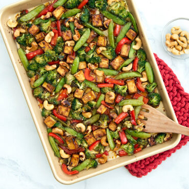 Roasted vegetables with cashews on Nordic Ware aluminum half sheet pan, featuring snap peas, red peppers, broccoli