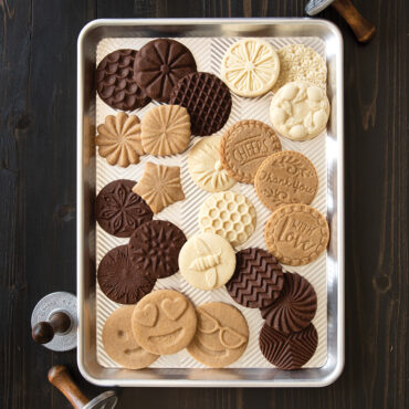 Golden baked cookies with decorative stamped patterns arranged on Nordic Ware aluminum half sheet pan