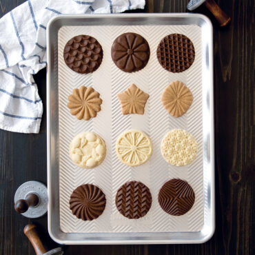 Golden baked cookies with decorative stamped patterns arranged on Nordic Ware aluminum half sheet pan
