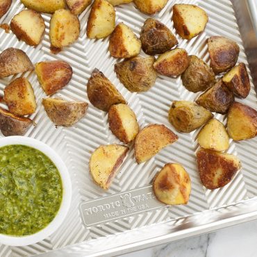 Golden roasted baby potatoes on Nordic Ware aluminum Prism half sheet with ridged surface and green herb sauce